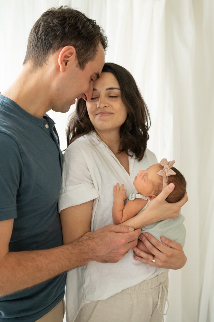 Parents looking down at sleeping newborn in soft lifestyle newborn studio setup.