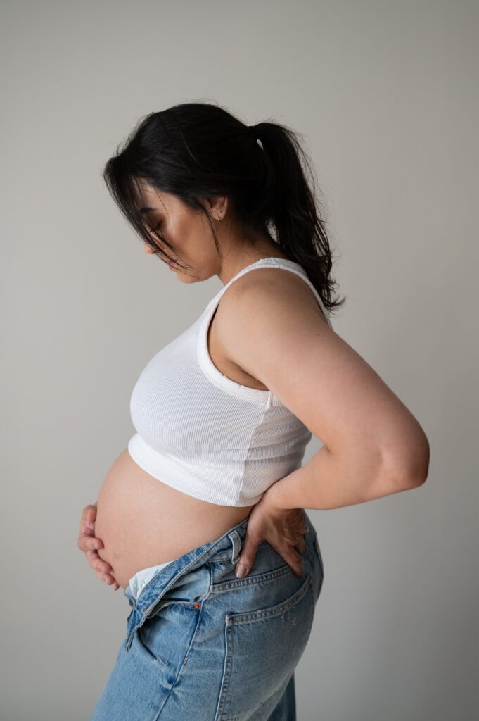 Mom sitting on a stool in natural light studio for minimal maternity pictures.