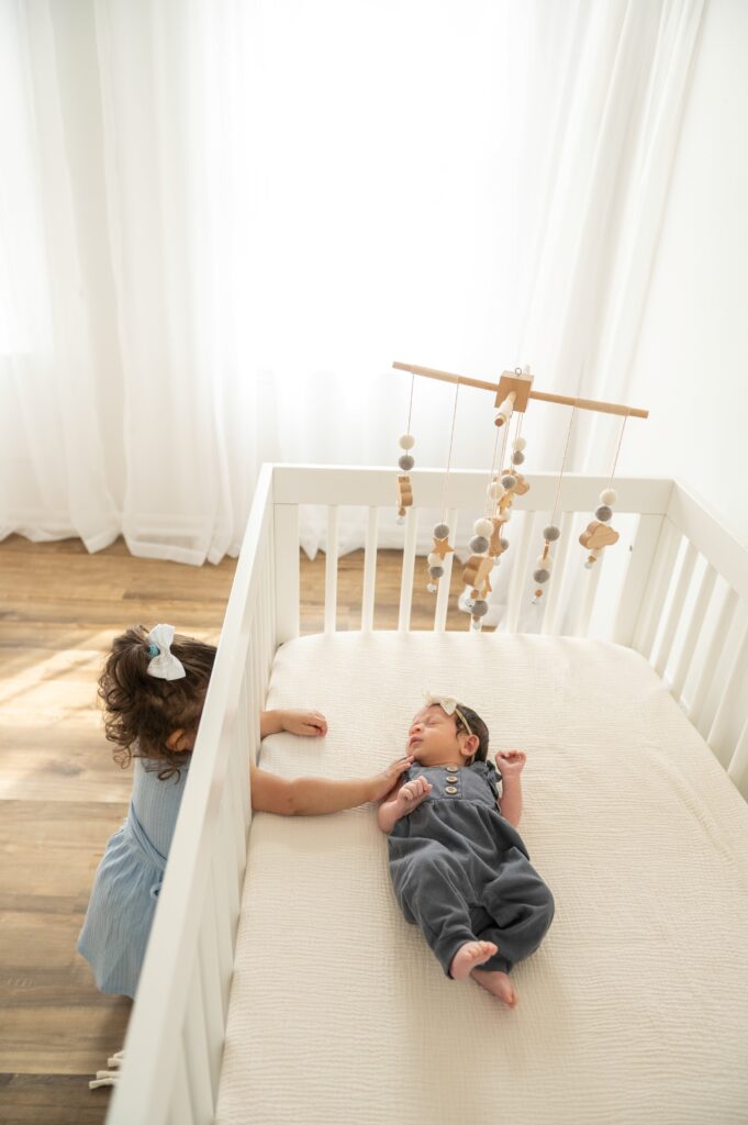 Older sibling gently holding newborn on bed in cozy home like studio.